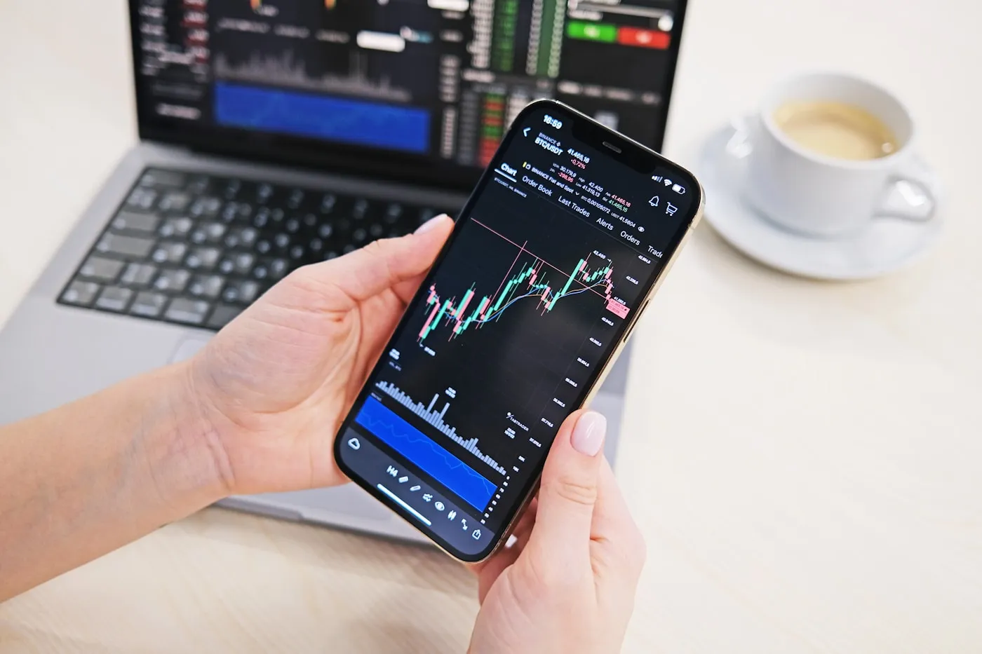 Two phones and a laptop showing trading screens on a desk